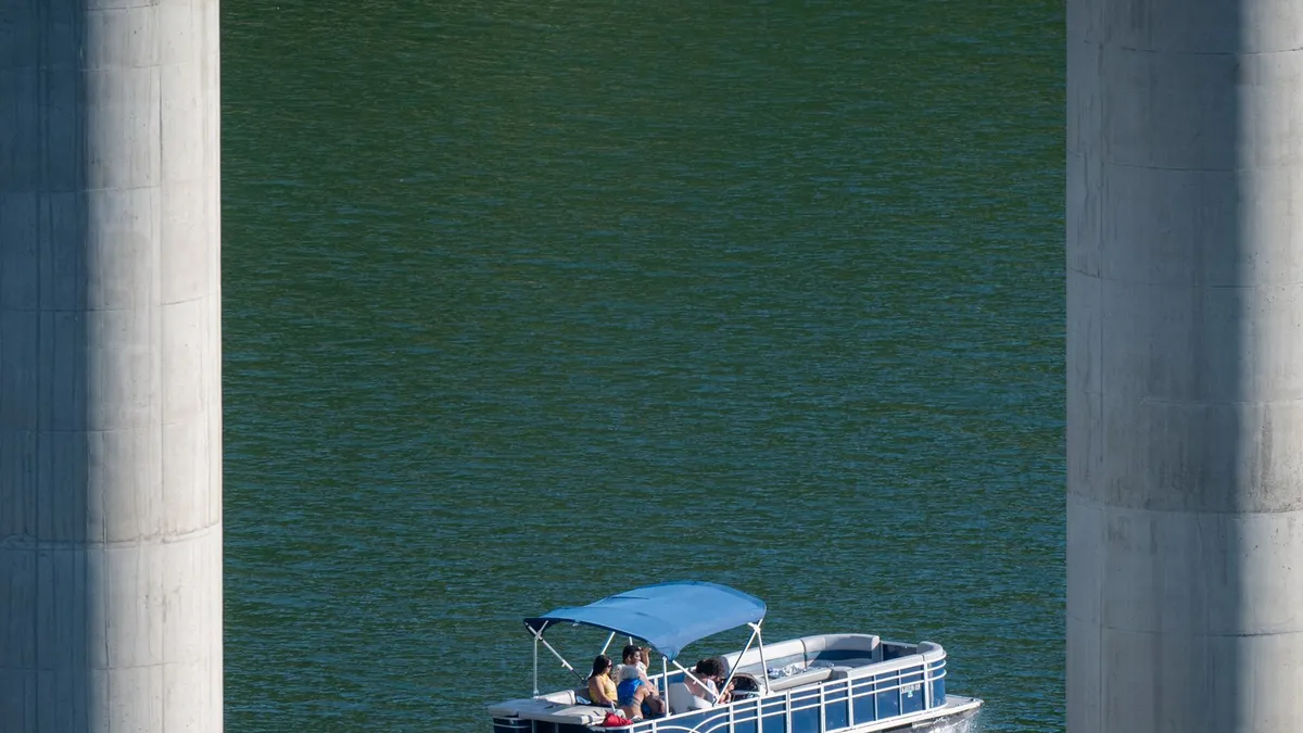 A pontoon boat passing between bridge pillars on green water