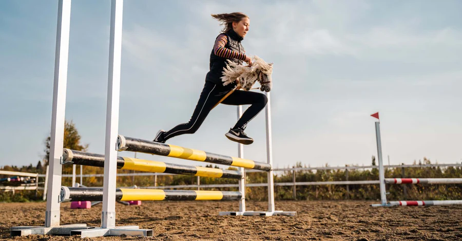 A hobbyhorser leaps over a hurdle.